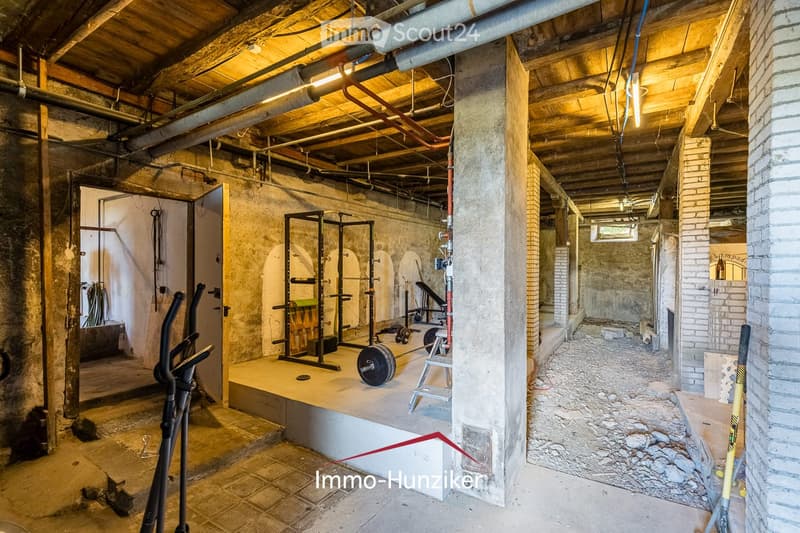 Unfurnished basement with exposed wooden beams, concrete walls, and a small workout area with gym equipment.