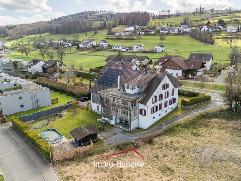 Aerial view of a residential house with a swimming pool, surrounded by greenery and neighboring houses in a rural setting.