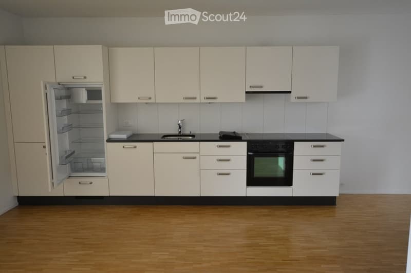 Modern kitchen with white cabinets, black countertops, and wooden flooring. Features include a refrigerator, microwave, sink, faucet, and oven.