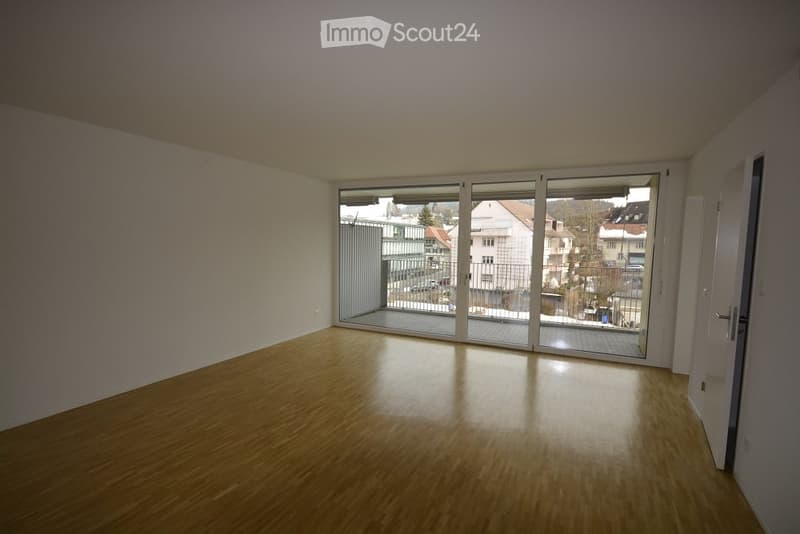 Empty room with wooden flooring, large sliding glass doors leading to a balcony, and white walls.
