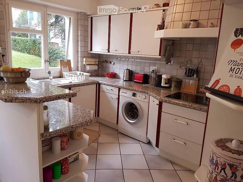Bright kitchen with white cabinets, granite countertops, and tiled backsplash. Includes a sink, dishwasher, washing machine, coffee maker, toaster, knife block, and various small appliances.