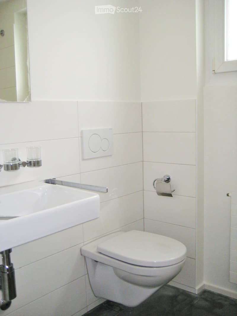 Modern bathroom with white tiles, a sink, toilet, mirror, and two cups on the sink counter.
