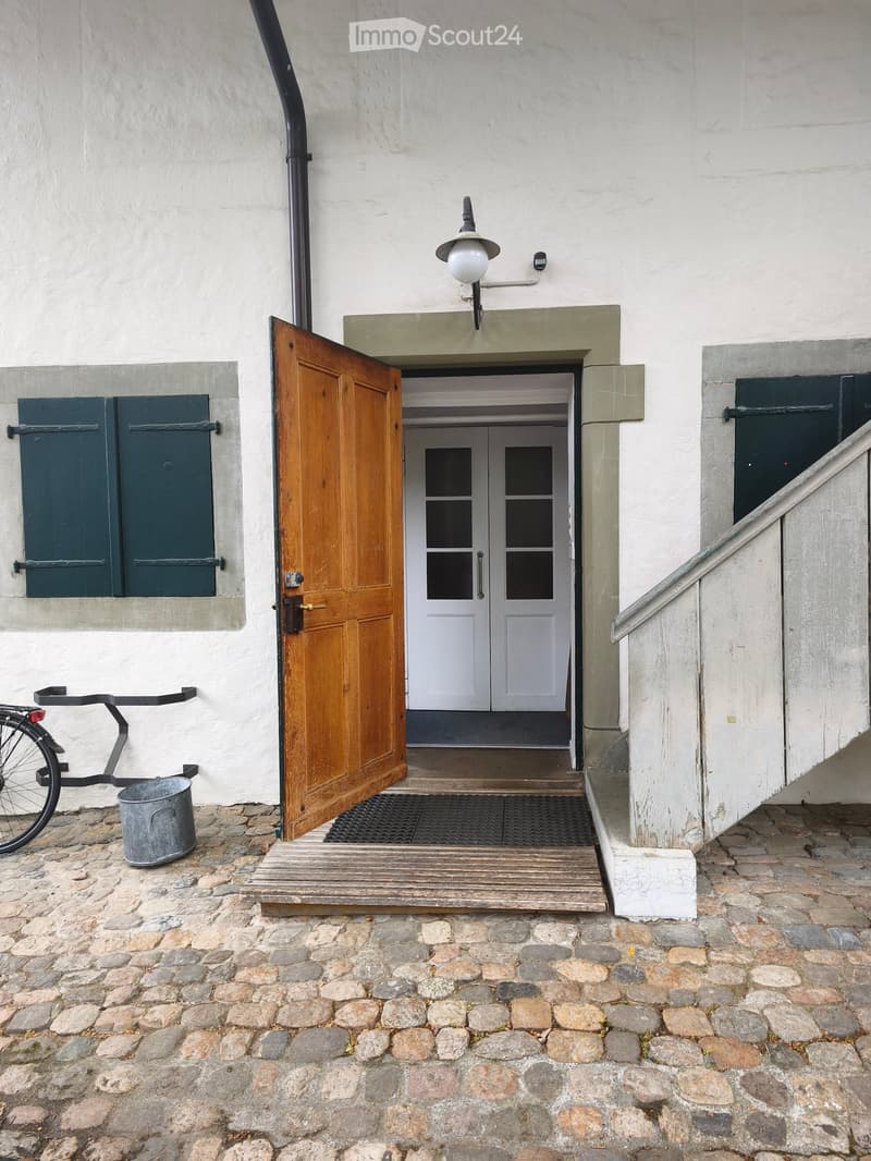 Entrance to a building with a raised wooden platform, a large wooden door, and a bicycle parked nearby.