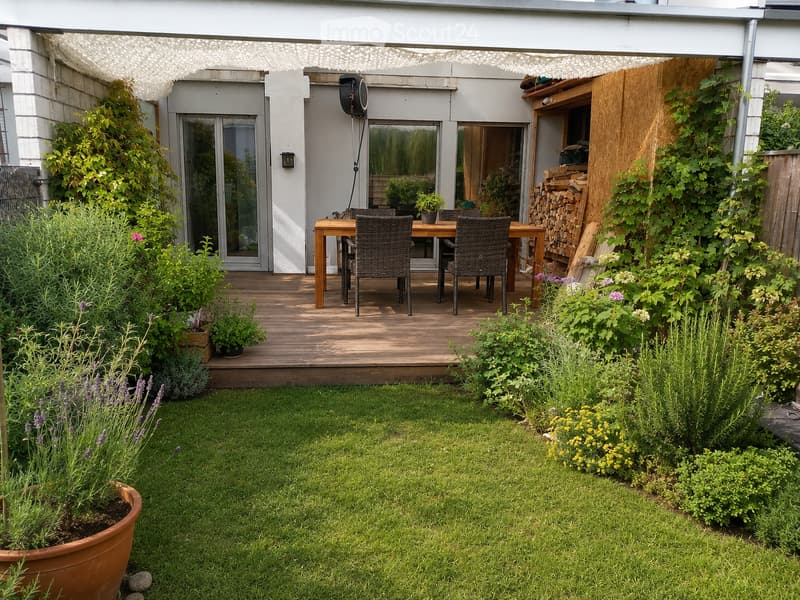 A well-maintained garden with a wooden deck, outdoor dining set, and lush greenery.