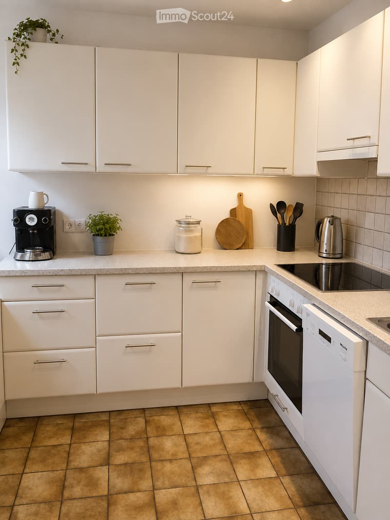 Modern kitchen with white cabinets, granite countertops, and various appliances including a coffee maker, oven, and dishwasher. The countertop features a potted plant, a glass jar, and a wooden cutting board.