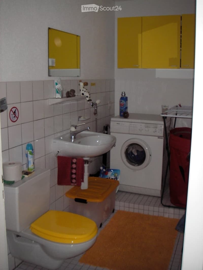 Bathroom with a sink, toilet, washing machine, yellow cabinets, and a mirror. Includes a towel, shelf, and various toiletries.