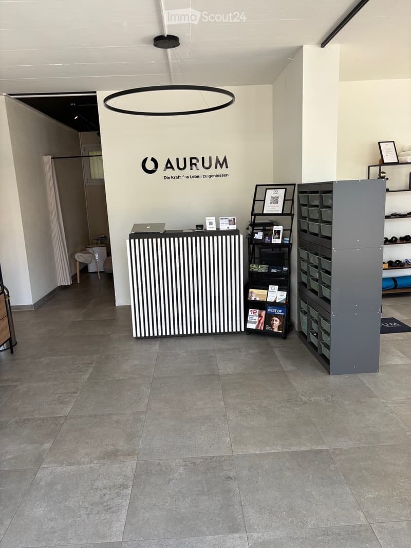 Modern reception area with a sleek reception desk, laptop, shelves with books and framed pictures, and a chair in the background.
