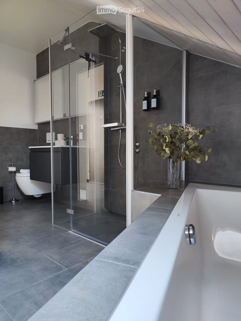 Modern bathroom with a large bathtub, glass-enclosed shower, toilet, and decorative vase with flowers on the counter.