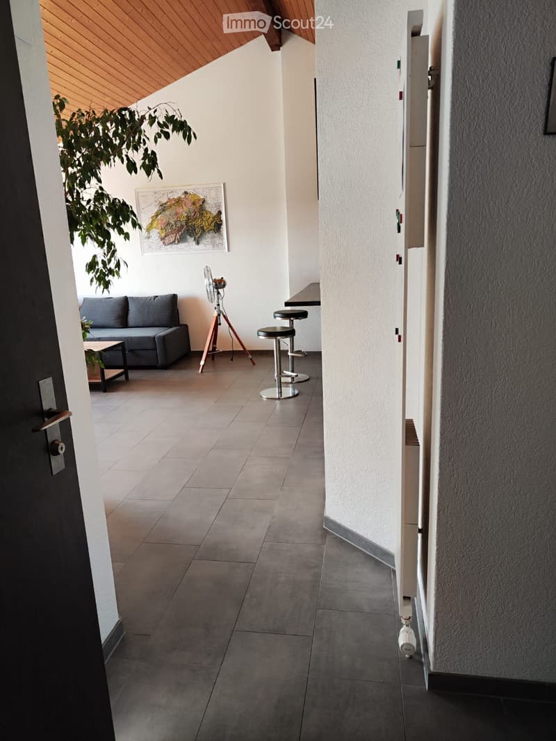 Modern hallway with a grey sofa, small table, two stools, a fan on a tripod, and a large map on the wall. The space has tiled flooring and white walls.