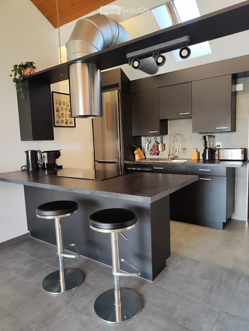 Modern kitchen with dark grey cabinets, stainless steel appliances, island with two bar stools, and various appliances on the counter.
