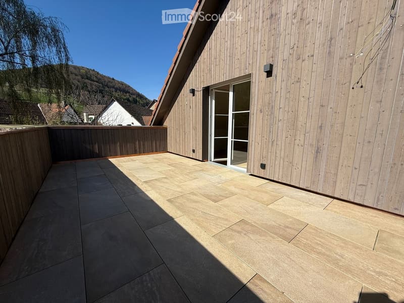 Balcony with tiled floor, wooden railing, and sliding glass door leading to the building.