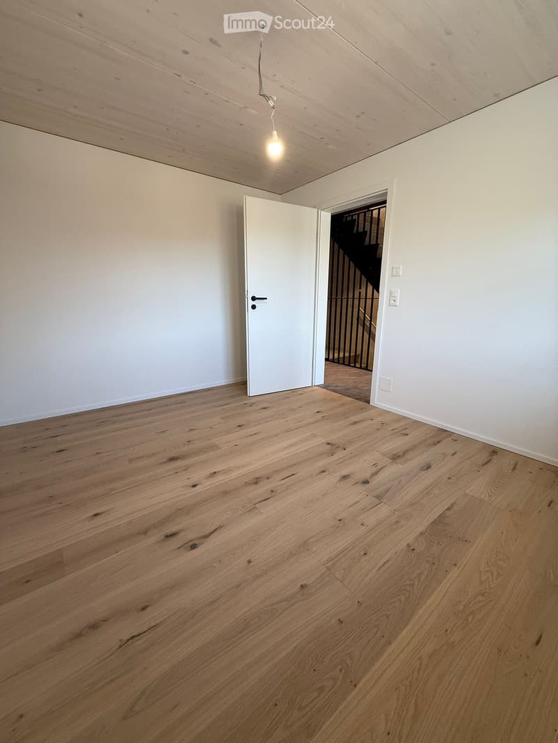 Empty room with light wooden flooring, white walls, and a single open door leading to a staircase area.