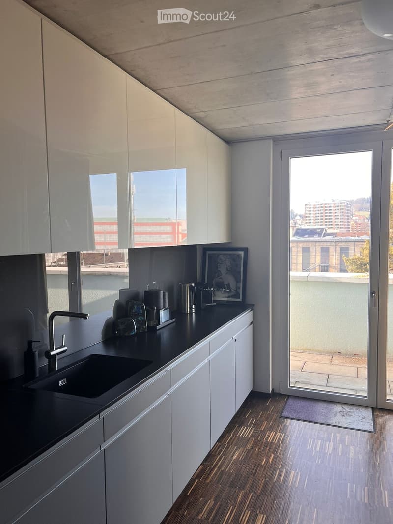 Modern kitchen with white cabinets, black countertop, and a sink. A picture frame and a cup are placed on the counter. The kitchen has a sliding glass door leading to a balcony with a city view.