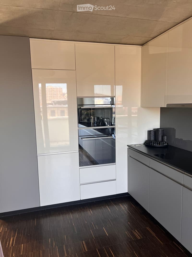 Modern kitchen with white cabinets, dark countertops, and a built-in oven. Features a sleek design with a dark wooden floor and a small decorative candle on the counter.