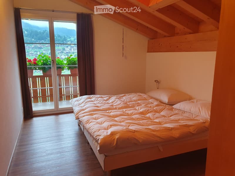 Cozy bedroom with wooden floor, large window offering a scenic mountain view, and a neatly made bed.