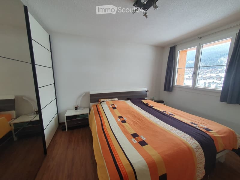 Bedroom with a large window offering a scenic mountain view, featuring a bed with a colorful striped duvet, a nightstand, a wardrobe, and a mirror.