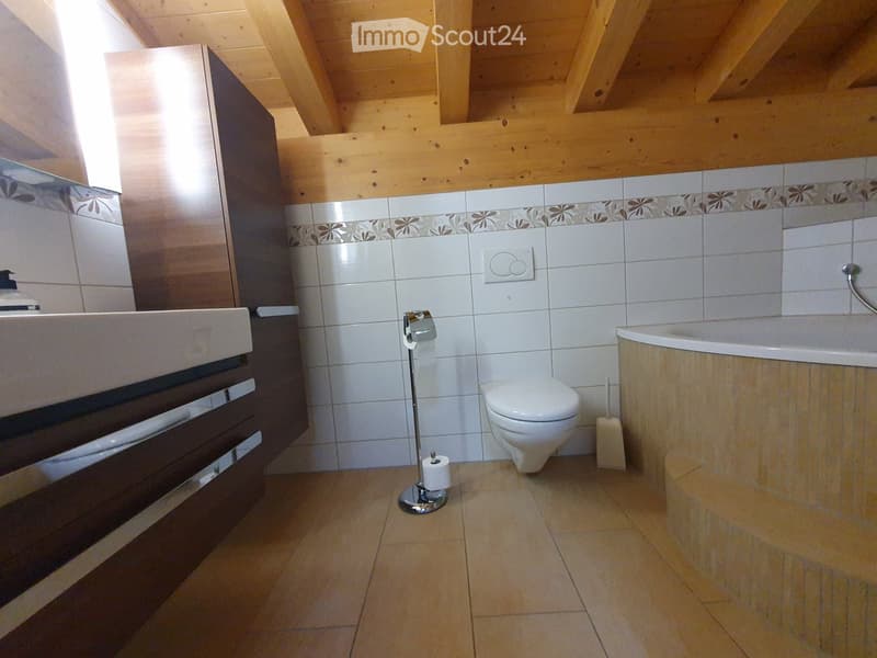 Modern bathroom with white tiles, a toilet, bathtub, sink, and a toilet paper holder. Wooden ceiling beams and a decorative border on the tiles.