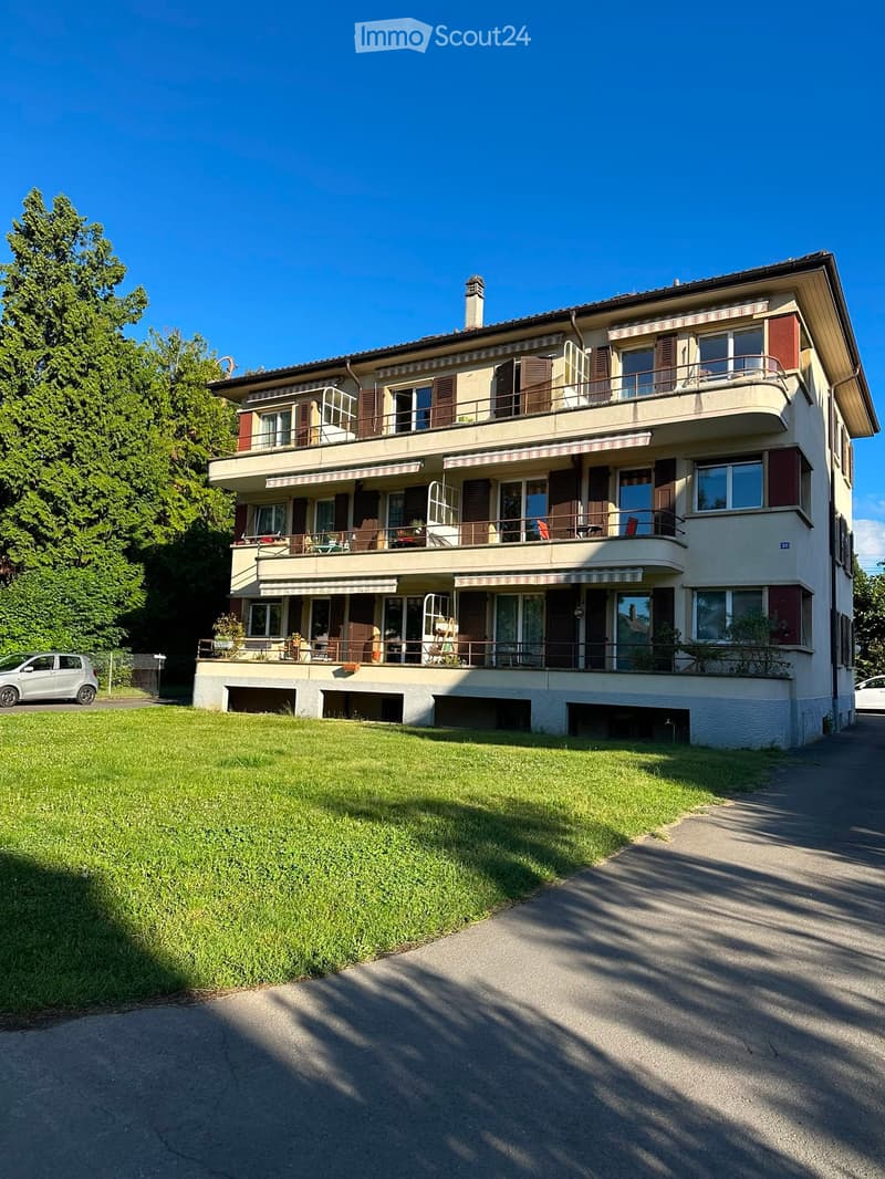 A three-story house with balconies, large windows, and a well-maintained lawn in front.