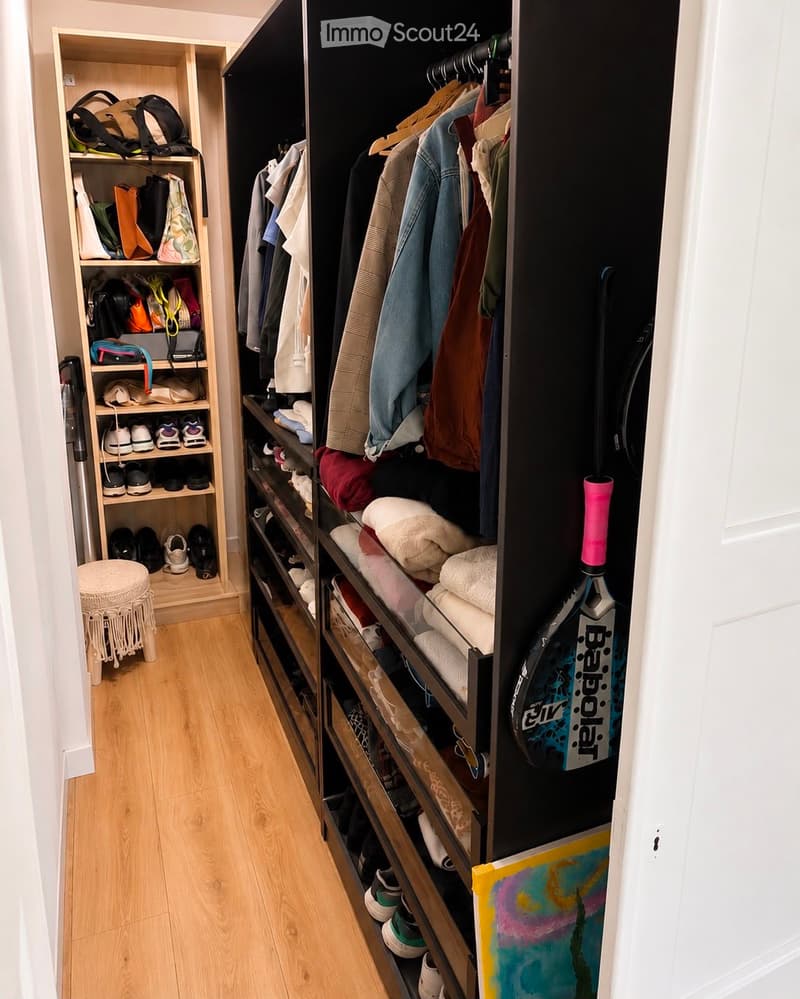 Well-organized walk-in closet with wooden flooring, built-in shelving, and storage compartments. Contains folded towels, shoes, bags, and a tennis racket.