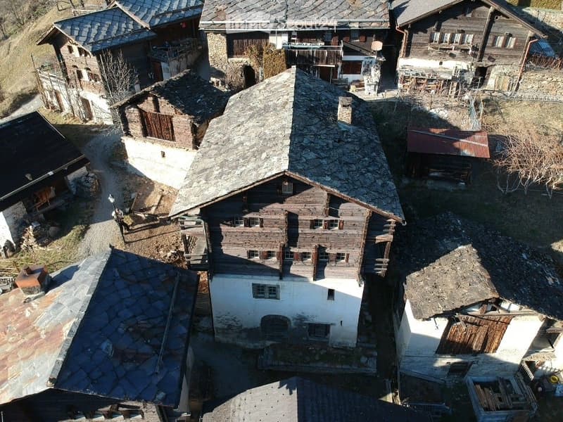 Aerial view of a rustic village with traditional wooden and stone houses, narrow pathways, and a mix of intact and partially dilapidated structures.