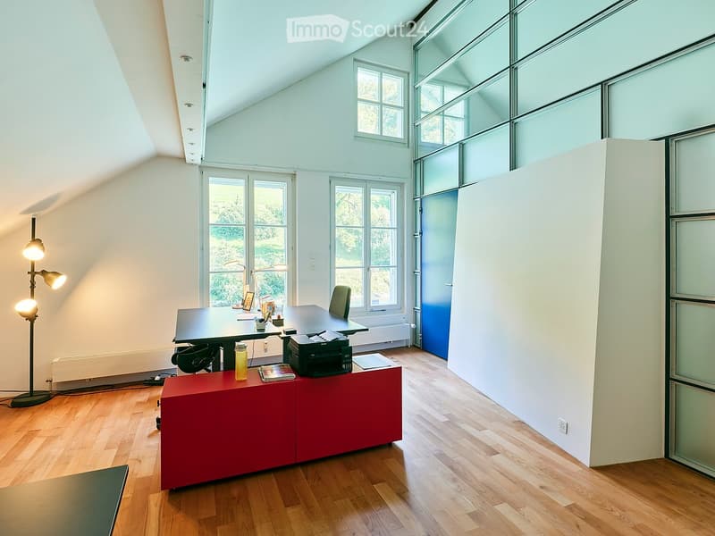 Bright, open room with wooden flooring, large windows, a desk with a chair, a printer, a red cabinet, and a floor lamp.