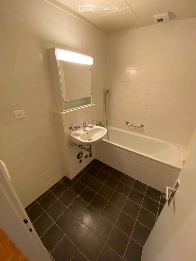 Modern bathroom with white tiles, dark grey floor tiles, a sink with a mirror, a bathtub, and a showerhead.