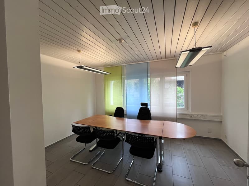 Modern office space with a large wooden table, several black chairs, and large windows with blinds.