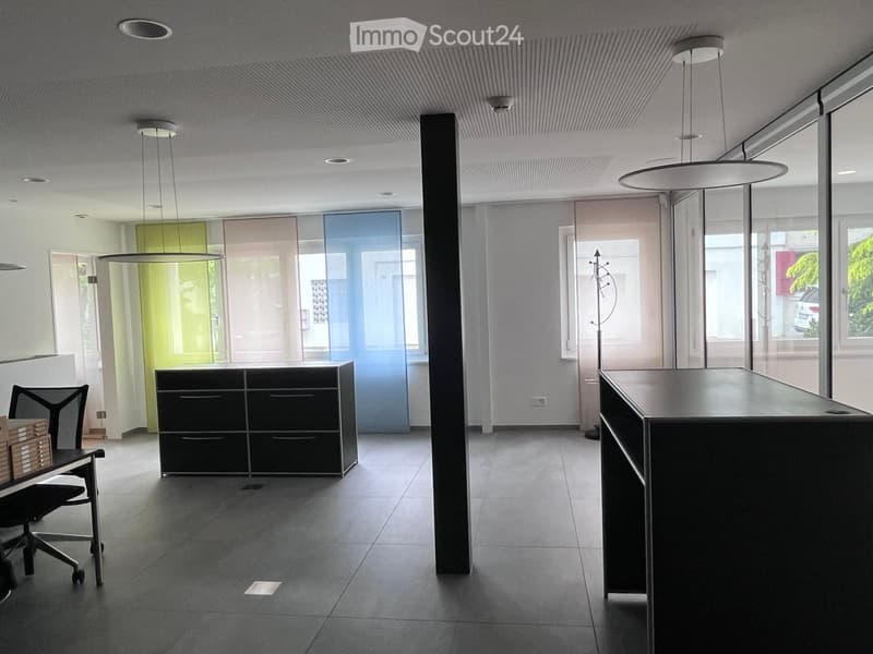 Modern office space with a sleek black desk, a black cabinet, a chair, and a coat rack near the entrance.