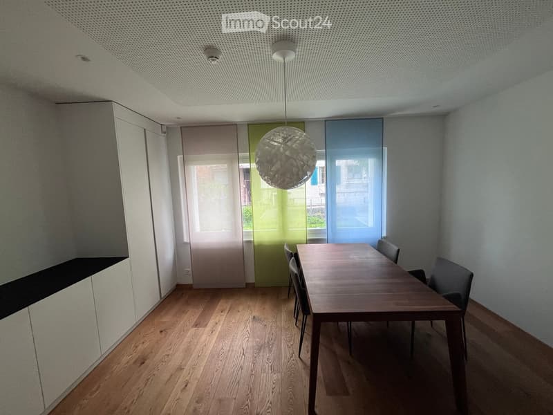 Modern dining area with wooden floor, large pendant light, dining table, and chairs.