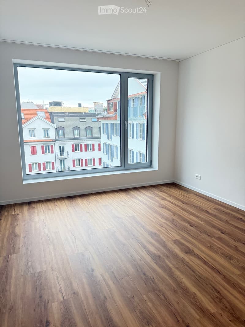 Empty room with wooden flooring and large window offering a view of the cityscape.