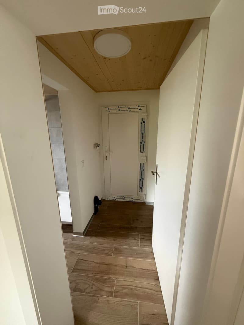 Empty hallway with wooden flooring, white walls, and a closed door at the end.