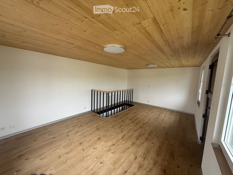 Empty room with wooden flooring, white walls, and a wooden ceiling. Features a staircase railing and recessed lighting.
