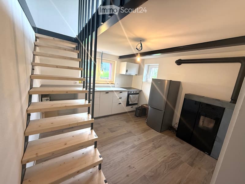 Modern kitchen with wooden flooring, white cabinets, stainless steel appliances, and a staircase leading upwards.