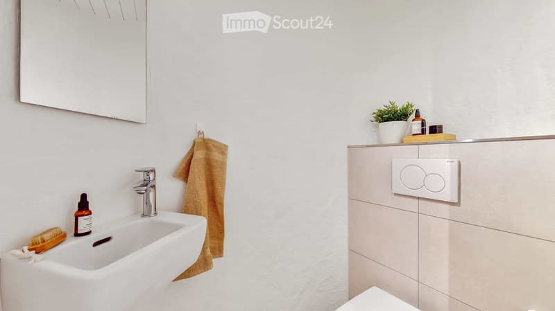 Modern bathroom with white tiles, a white sink, a chrome faucet, a large mirror, a beige towel, and a small plant on the counter.