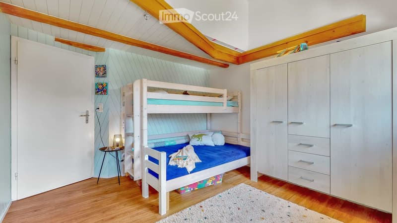 Cozy bedroom with a bunk bed, white wardrobe, small table with lamp, and a white rug on wooden flooring.