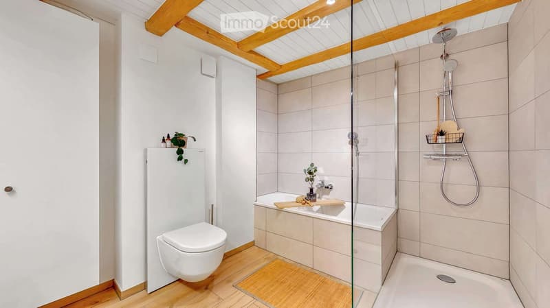 Modern bathroom with a toilet, bathtub, and shower area. Features wooden beams on the ceiling, a glass partition, and decorative plants on shelves.