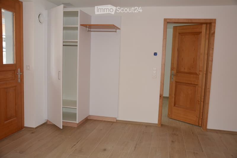 Empty room with light wooden flooring, white walls, and a built-in closet with shelves. Two wooden doors are visible, one leading to another room.