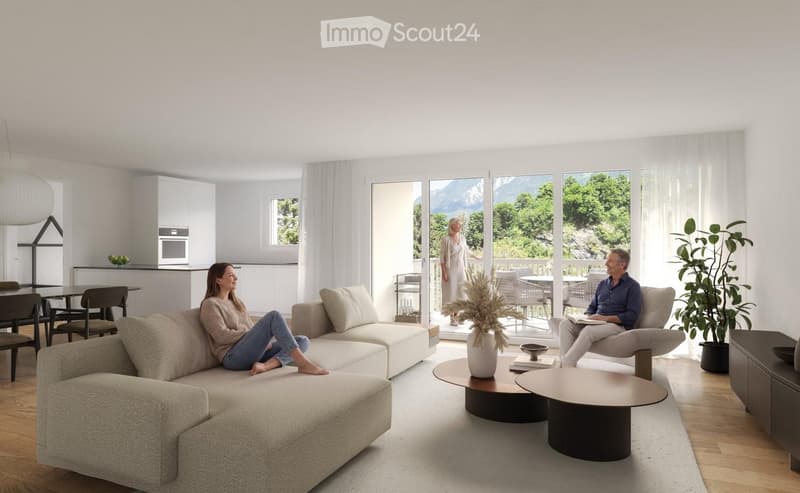 Bright living room with large windows offering a scenic mountain view. Features a beige sectional sofa, two coffee tables, a chair, a dining area with a table and chairs, and a kitchen area with cabinets and appliances.