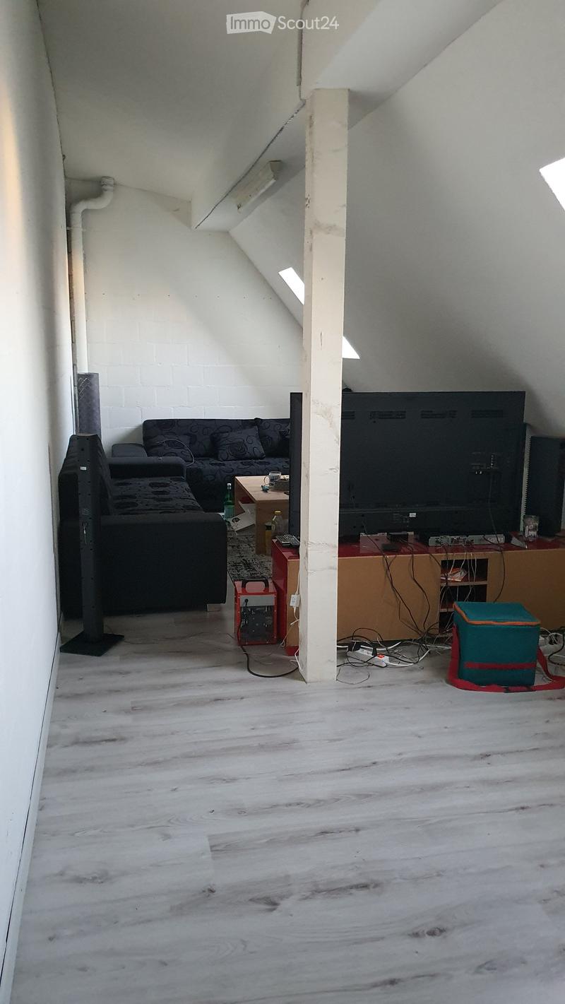 Living room with a sofa, coffee table, television, and various items on a table, including a cup and a bottle. The room has wooden flooring and white walls.