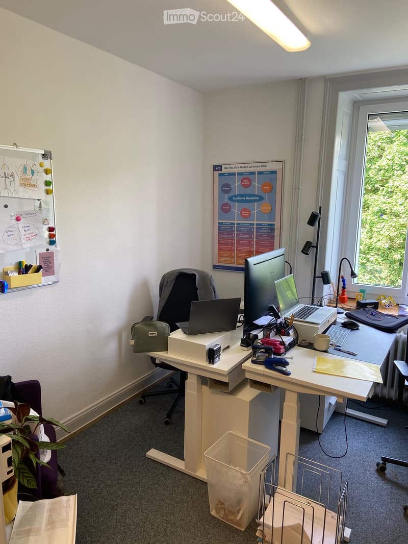 Office space with a standing desk, chair, laptop, screen, keyboard, mouse, cup, stapler, plant, book, whiteboard, and poster on the wall.