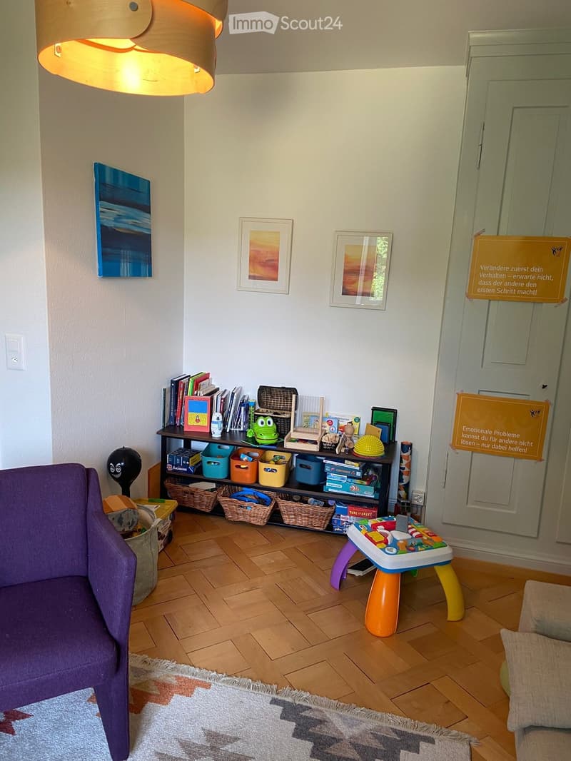 A cozy children's room with a purple sofa, a shelf filled with books and toys, a small toy table, and colorful baskets on the floor.