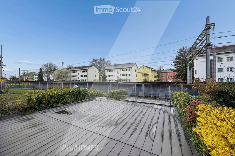 wooden deck, plants, flowers, fence, buildings in the background