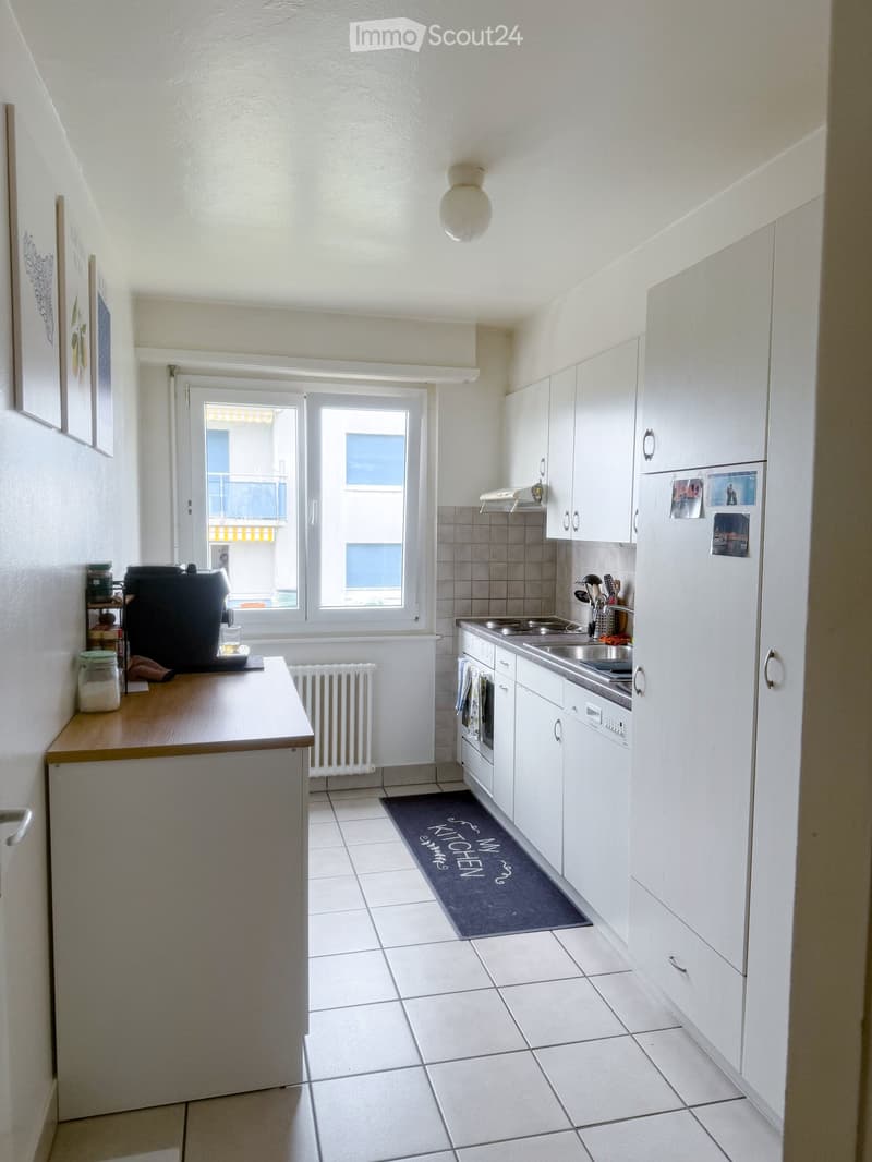 Modern kitchen with white cabinets, stainless steel appliances, tiled floor, and a small island with a coffee maker and jars.