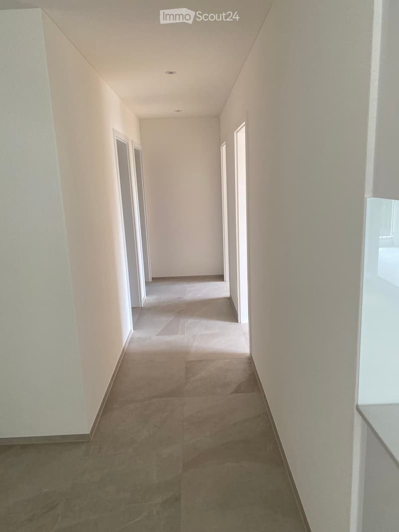 Empty hallway with beige walls, tiled floor, and several doors on both sides.