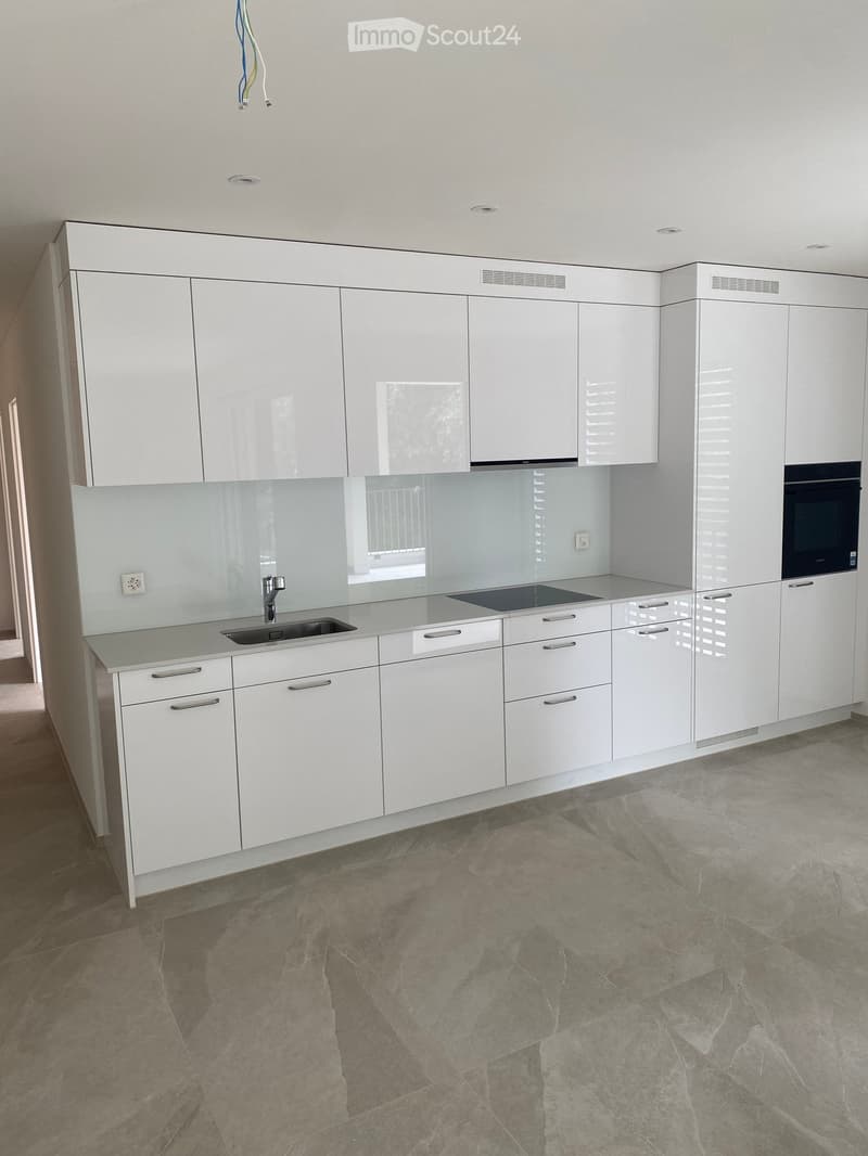 Modern, minimalist kitchen with white cabinets, a sink, and an oven. The countertops are light-colored, and the floor is made of polished stone tiles.