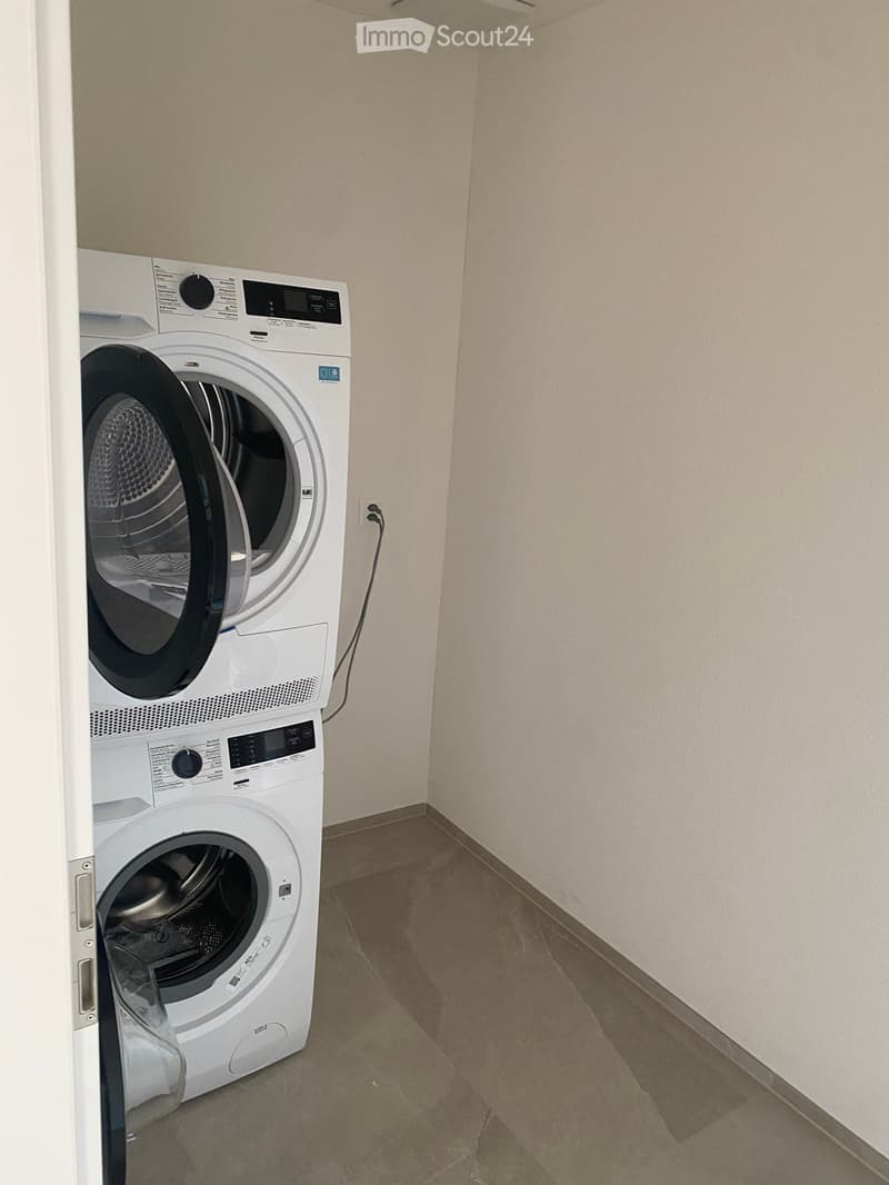 A small room with a washing machine and dryer stacked vertically, white walls, and a tiled floor.