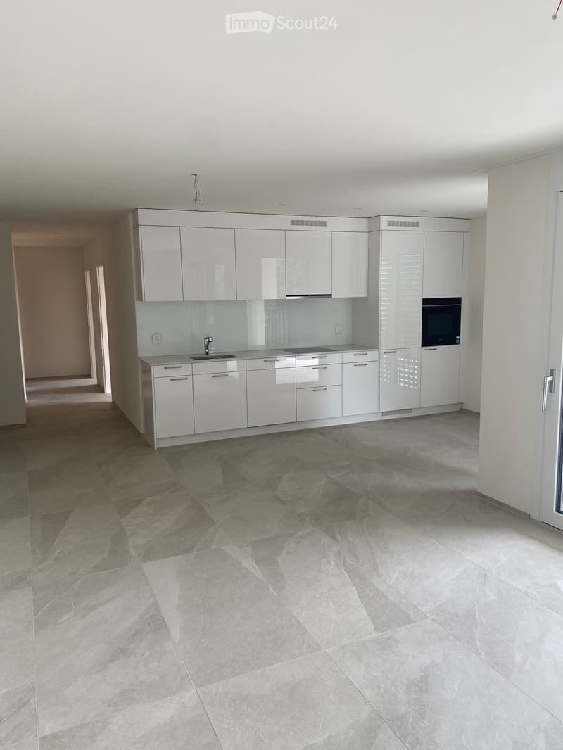 Modern, minimalist kitchen with white cabinets, a sink, and an oven. The floor is tiled with large, polished stone tiles.