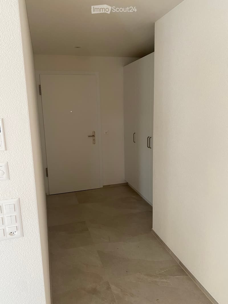 Empty hallway with tiled floor, white walls, and a closed door at the end.