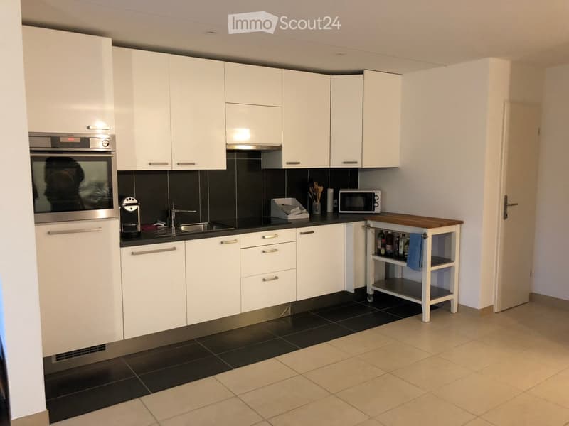 Modern kitchen with white cabinets, stainless steel oven, microwave, coffee maker, and a small wooden kitchen island with shelves.