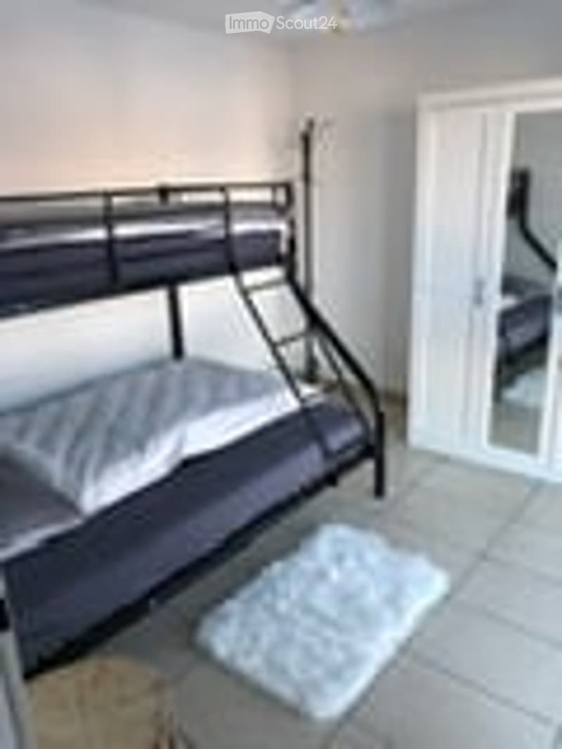 A bedroom with a dark-colored bunk bed and a white rug on the floor. The room has light-colored walls and a glass door leading to another space.